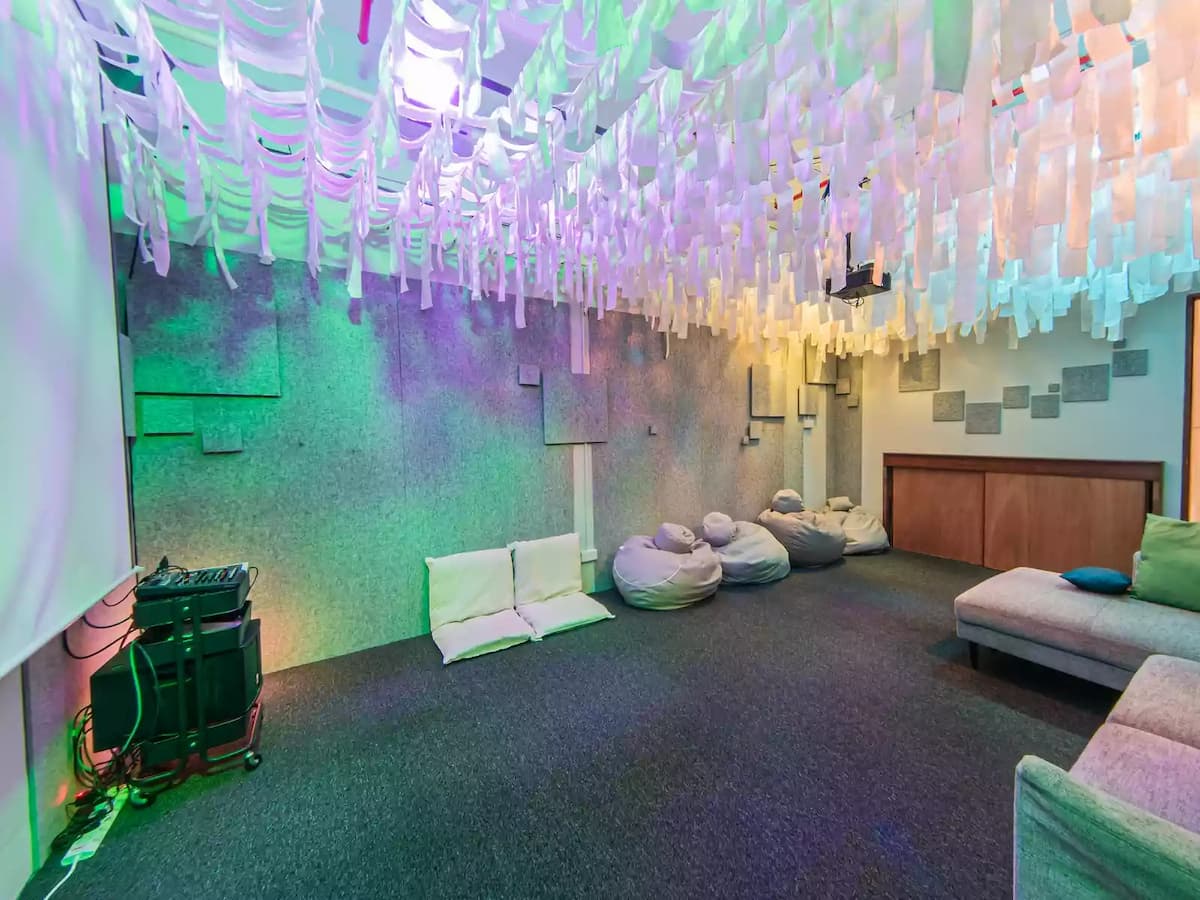 Creative immersive lounge space with hanging fabric ceiling installations, soft seating, bean bags, and a projector screen—ideal for workshops, film screenings, brainstorming sessions, team retreats, or interactive presentations.