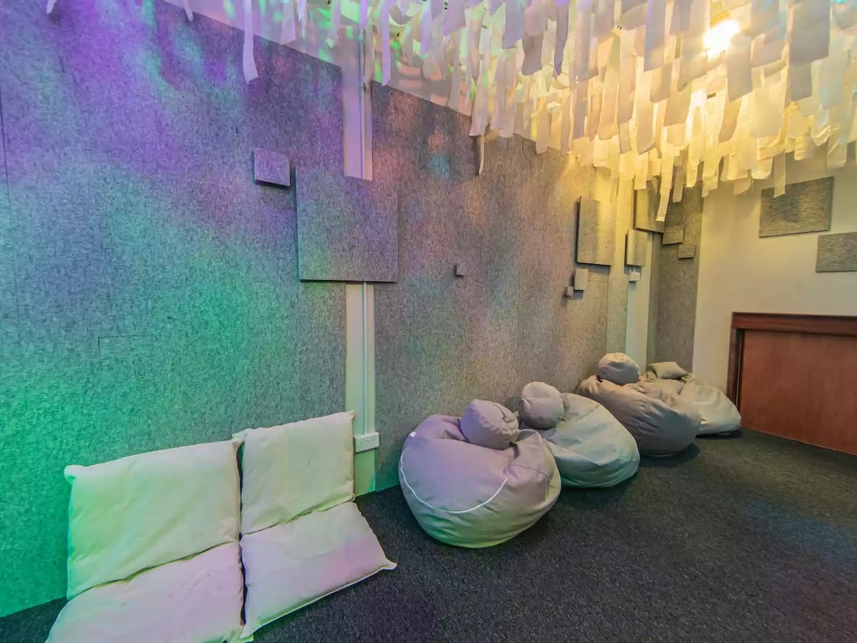 Creative immersive lounge space with hanging fabric ceiling installations, soft seating, bean bags, and a projector screen—ideal for workshops, film screenings, brainstorming sessions, team retreats, or interactive presentations.