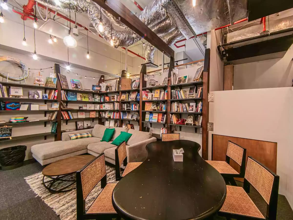 Cozy creative lounge and library-style space featuring bookshelves, a sofa seating area, and a meeting table—ideal for small workshops, team discussions, book clubs, creative brainstorming sessions, or intimate community events.