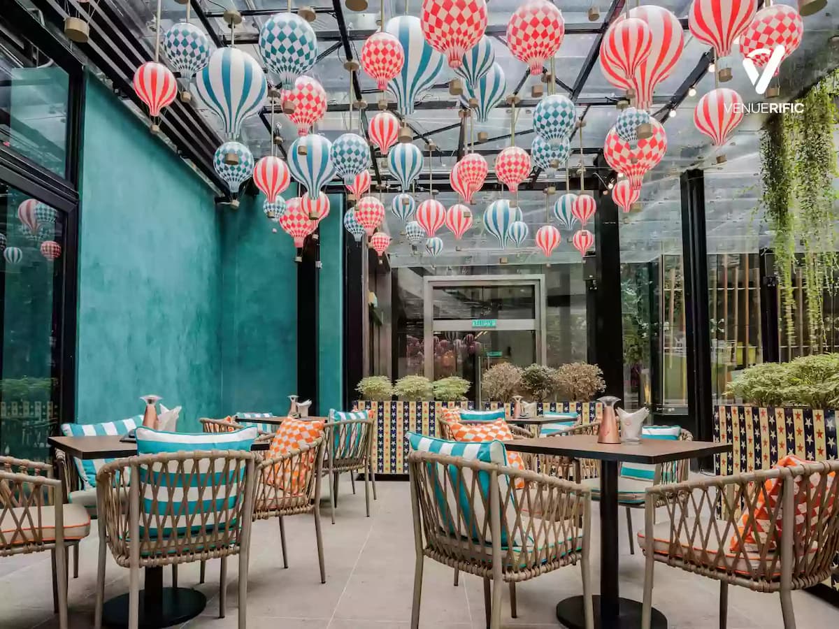 Bright glass-enclosed dining space with colorful hot air balloon decor and rattan seating for casual gatherings.