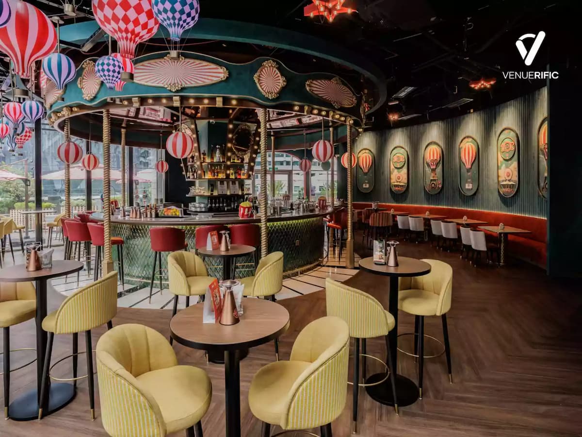 Vibrant carnival-themed bar with hot air balloon decor, colorful seating, and a central carousel-style counter.