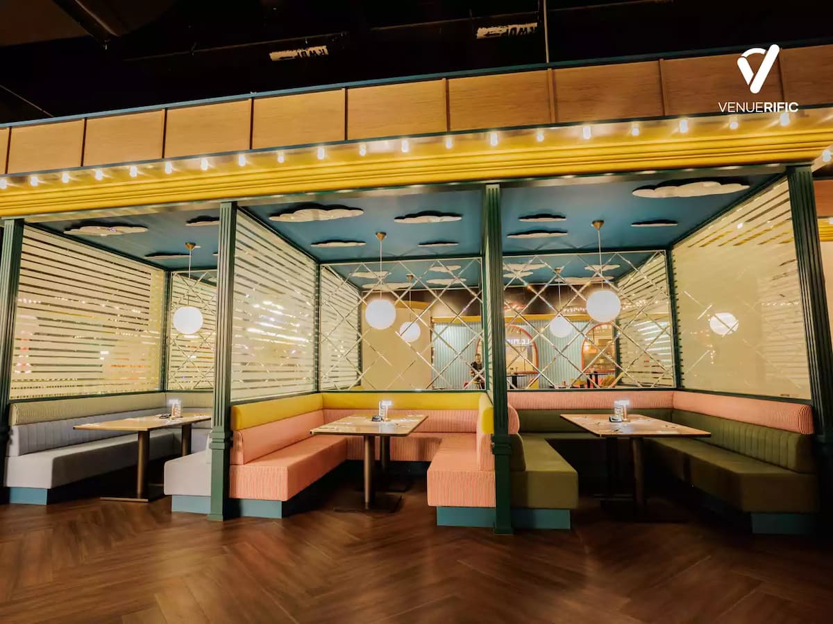 Colorful semi-private booth seating with pastel cushions, glass partitions, and warm ambient lighting for intimate dining.