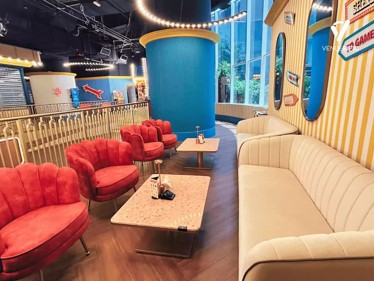 Colorful lounge corner with striped walls, neon game signage, plush seating, and marble tables for casual gatherings.