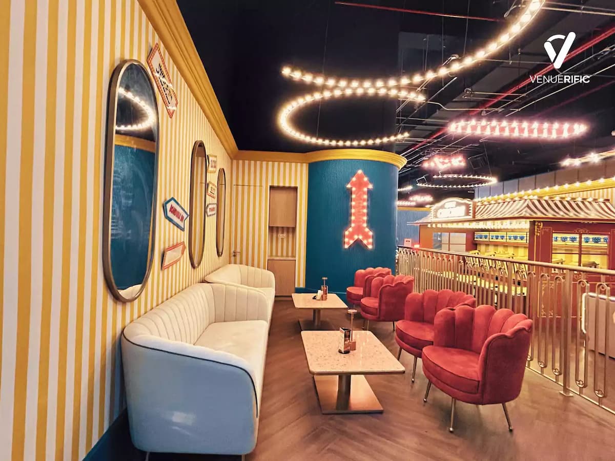 Colorful lounge corner with striped walls, neon game signage, plush seating, and marble tables for casual gatherings.