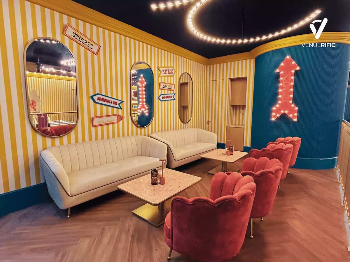 Colorful lounge corner with striped walls, neon game signage, plush seating, and marble tables for casual gatherings.