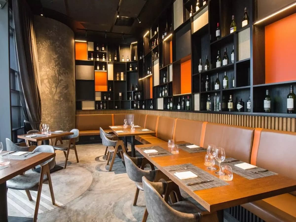 Elegant restaurant seating with long wooden table, leather banquette, wine bottle display wall, and warm accent lighting.