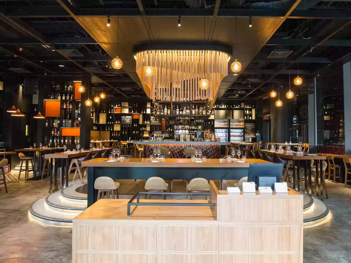 Upscale restaurant interior with wooden tables, leather chairs, warm pendant lighting, and a stylish open kitchen backdrop.