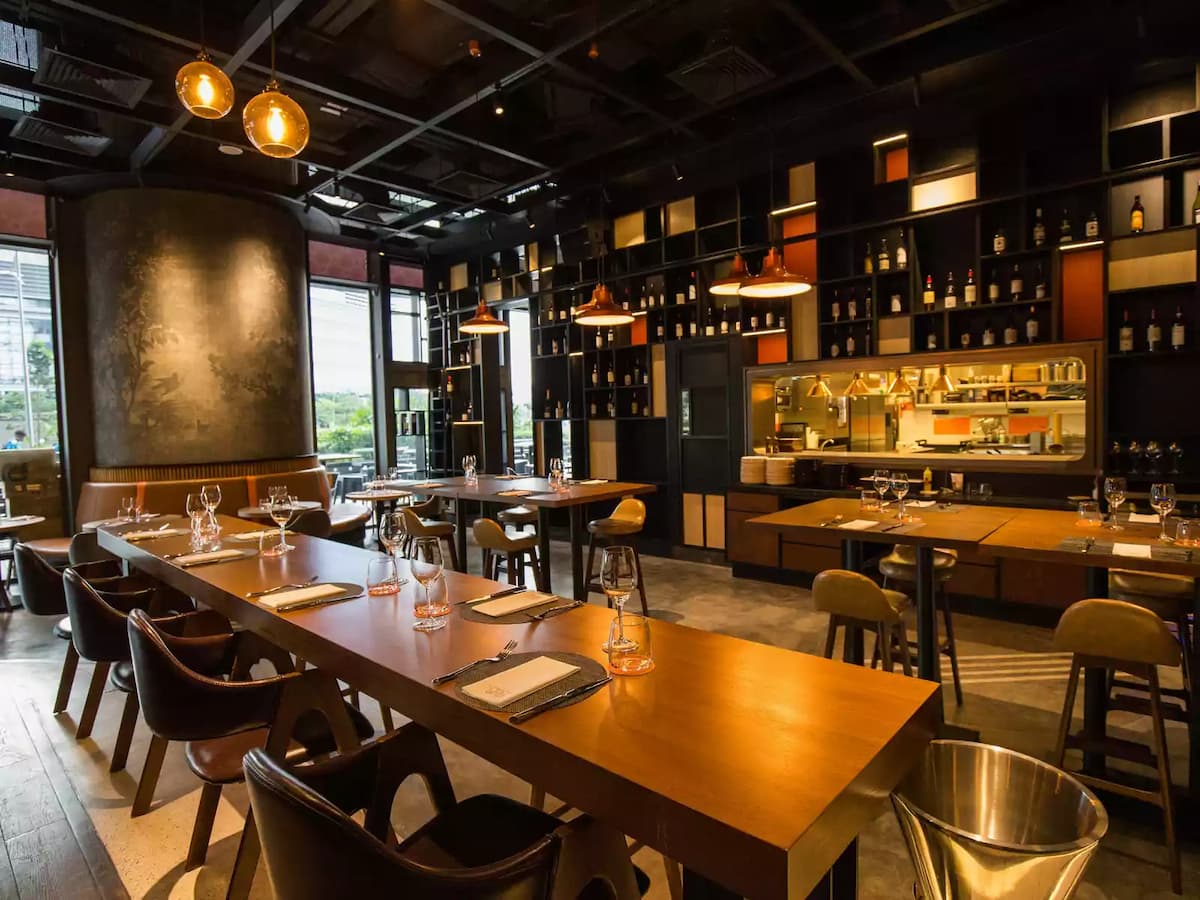 Upscale restaurant interior with wooden tables, leather chairs, warm pendant lighting, and a stylish open kitchen backdrop.